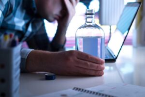 An employee sits at his desk with a bottle of alcohol. Using a employee reasonable suspicion observation checklist helps document these cringe-worthy events.