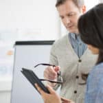 Two managers discuss a property inspection report form on a mobile device.