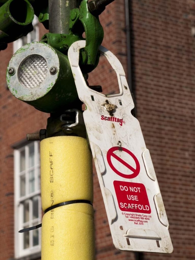 A red 'Do Not Use' tag is shown attached to a vertical scaffold pipe in this job site photo.