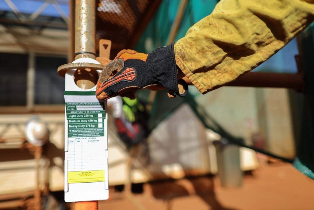 A green scaffold tag with white background is shown in this job site photo.