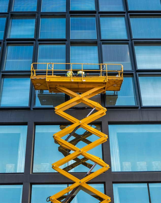 A scissor lift is shown beside an office building.