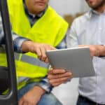 A manager shows a driver how to use the checklist for forklift inspection on a mobile device