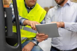 A manager shows a driver how to use the checklist for forklift inspection on a mobile device