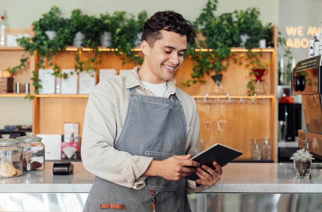 A barista holds a tablet with the 1st Reporting app and the restaurant health inspection checklist.