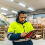 A warehouse worker completes a health and safety risk assessment form on a tablet.