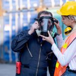 A safety manager helps a team member with a respirator after using the Respirator Inspection Checklist by 1stReporting.com.