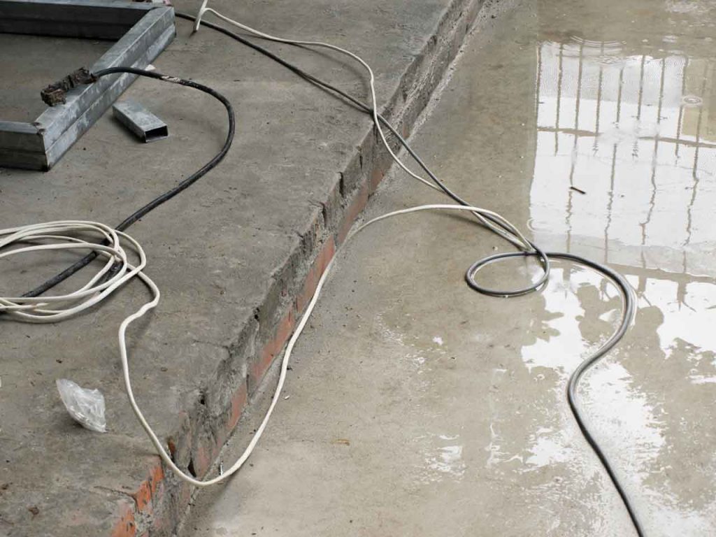 Wet conditions pose multiple risks, as shown in this image of electrical cabling on a wet concrete floor. Track near misses and other hazards using 1stReporting.com.