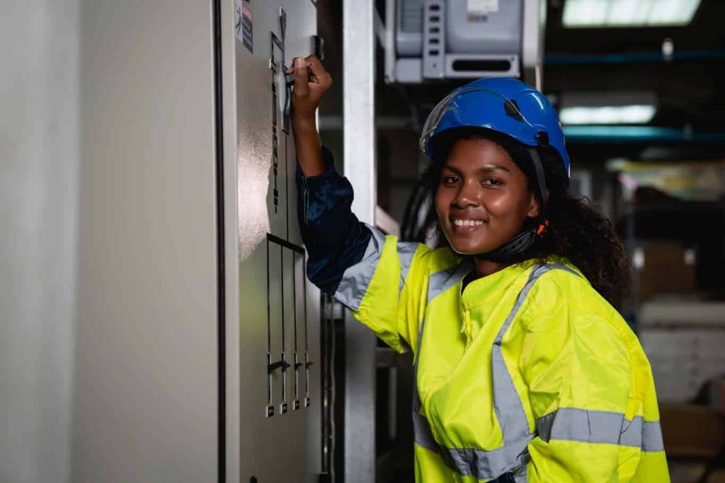 A maintenance worker happily controls a breaker panel knowing that her team confidently uses custom forms in the 1st Reporting app to make their work safer. Learn more at 1stReporting.com.