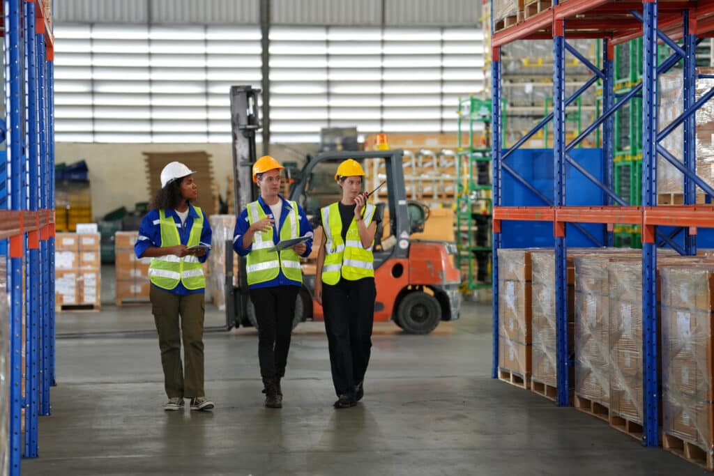Three safety officers walk through a warehouse, learning with the warehouse safety guide by 1st Reporting.