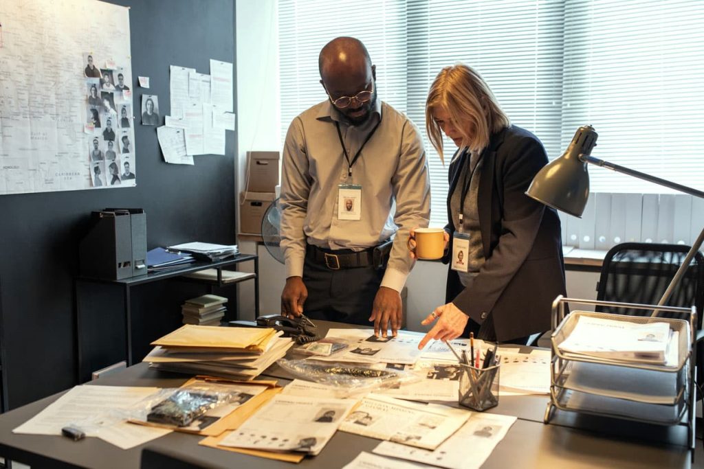 Two investigators peruse a mountain of paperwork. Learn how you can reduce your paperwork with 1stReporting.com.