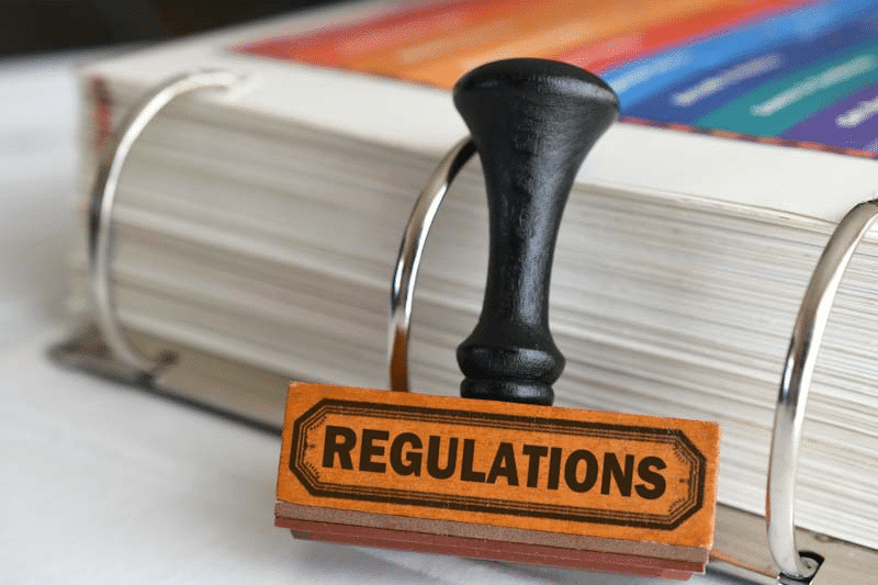 A stamp labeled 'Regulations' and a thick binder represent the current state of industry safety compliance. Learn more about mobile reporting for industry compliance at 1stReporting.com.