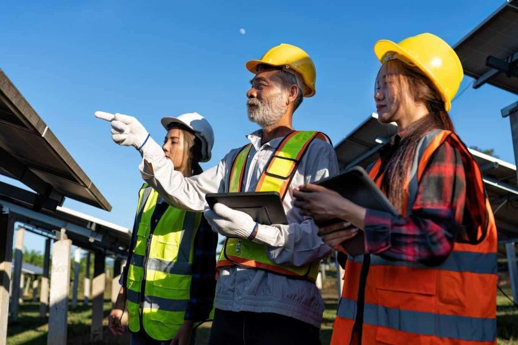 Three construction officers working with tablets at a solar installation construction site. Learn about using a digital construction change order form at 1stReporting.com.