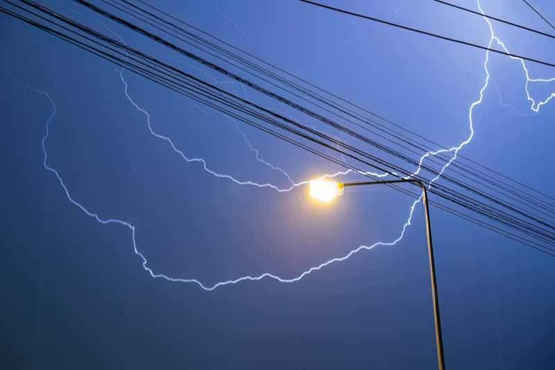 Lightning shown behind power lines and a street light representing the power of the 2022 Derecho storm event in Canada.